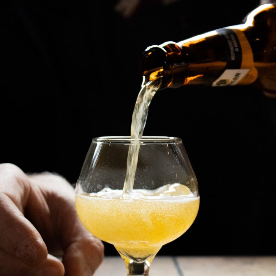 Light beer pouring from a bottle into a stemmed glass, creating foam.