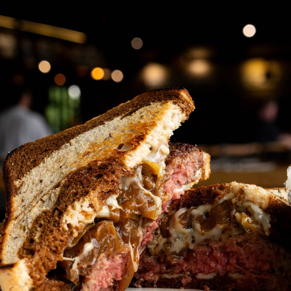 Close-up of a cut patty melt sandwich with caramelized onions, melted cheese, and toasted rye bread.