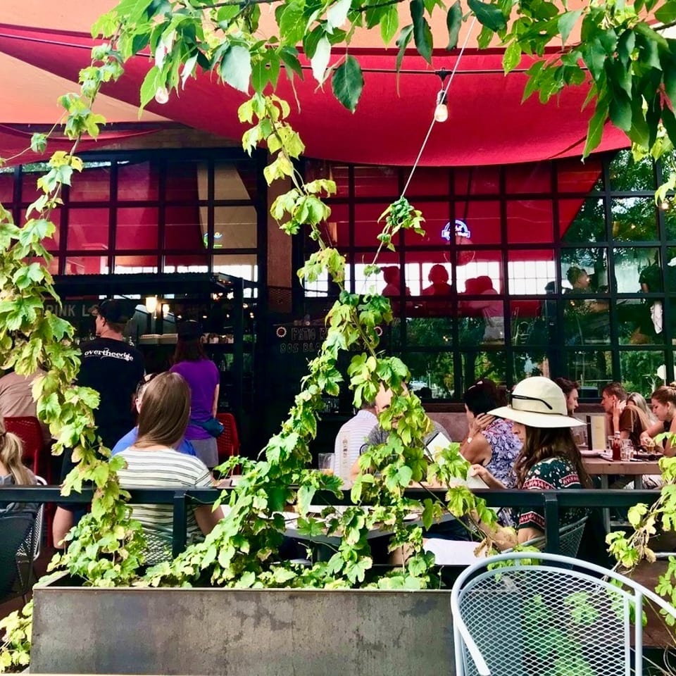 Diners enjoying an outdoor restaurant patio with red awnings and lush green vines.
