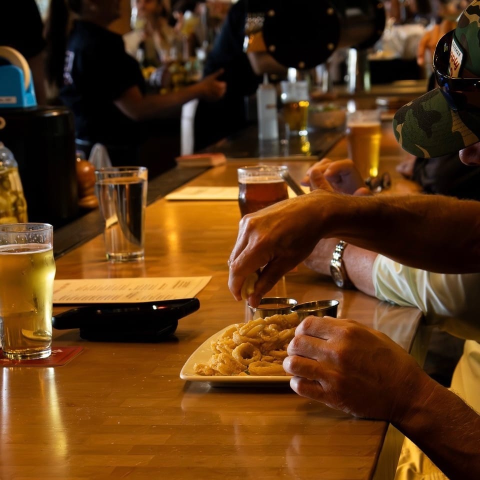 A person squeezes lemon over a plate of fried calamari at a busy bar with drinks.