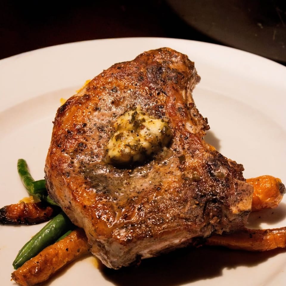 Grilled pork chop topped with herb butter, served with green beans and roasted carrots.