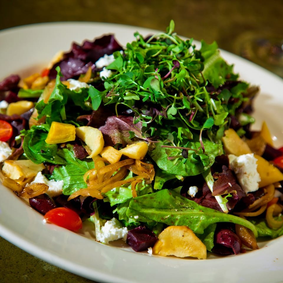 A vibrant salad with mixed greens, cherry tomatoes, beets, goat cheese, and microgreens.