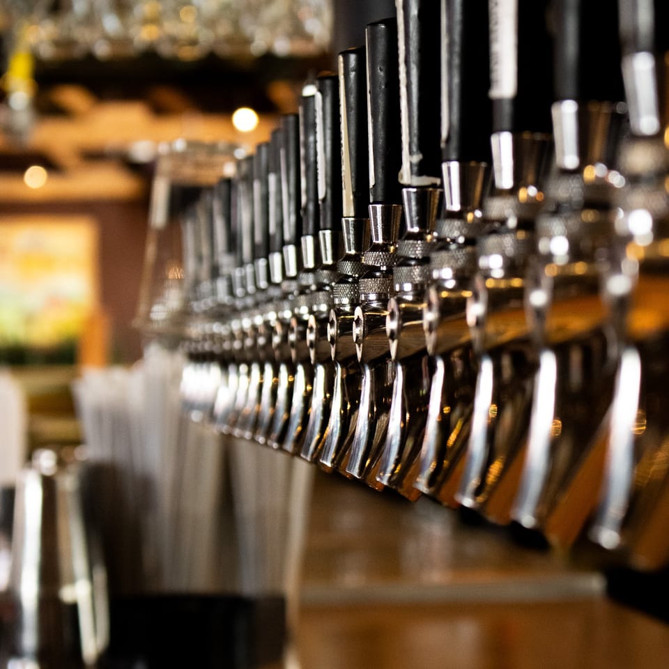 A long row of shiny beer taps in a dimly lit bar.