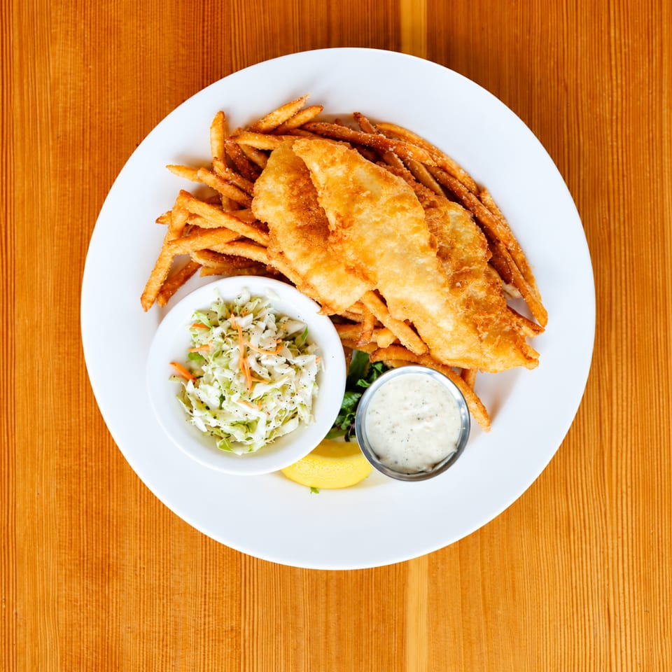 Fried fish and chips with coleslaw, tartar sauce, and a lemon wedge on a white plate.