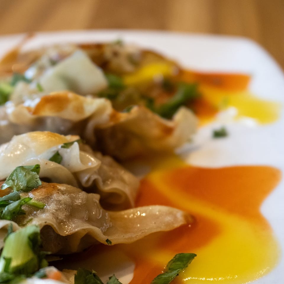 Close-up of pan-fried dumplings with green herbs, orange and yellow sauces, and coleslaw.