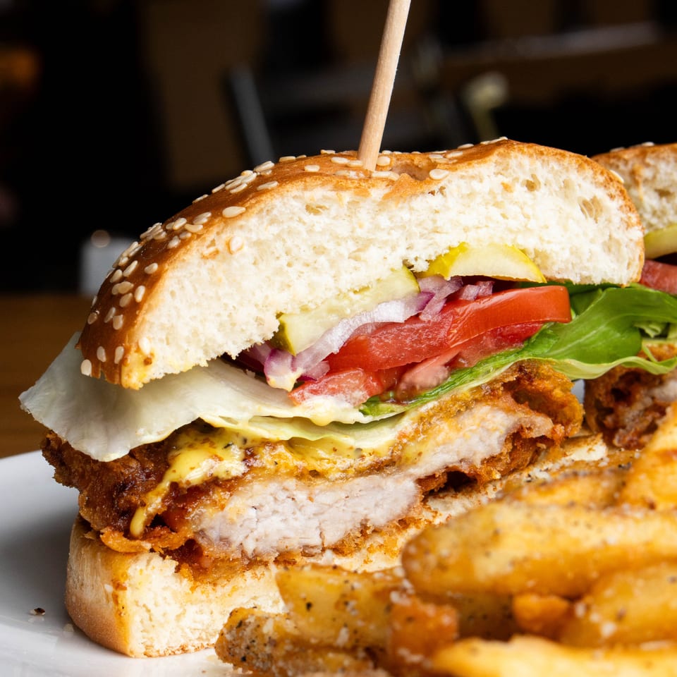 Half-eaten fried chicken sandwich with lettuce, tomato, onion, pickles, and a side of fries.