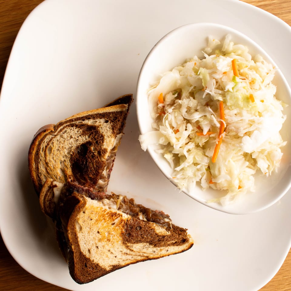A toasted sandwich on marble rye bread with a side of coleslaw on a white plate.
