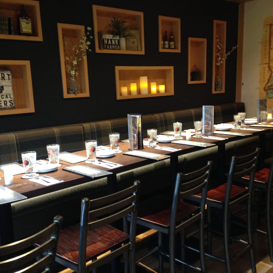 Cozy restaurant interior with long booth seating, high tables, and rustic wall decor.