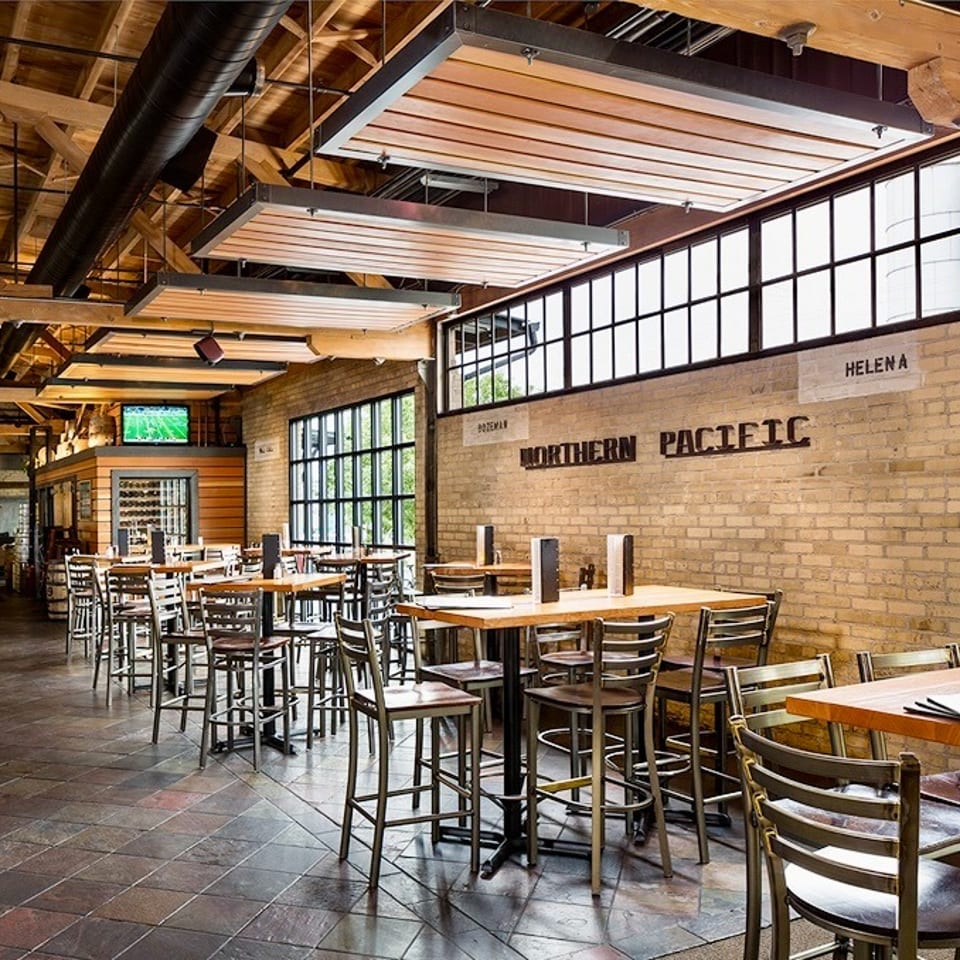 Industrial-style restaurant interior with high-top tables, brick wall, and "Northern Pacific" sign.