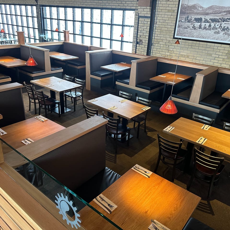 Restaurant dining room with wooden tables, booths, red pendant lights, and large windows.