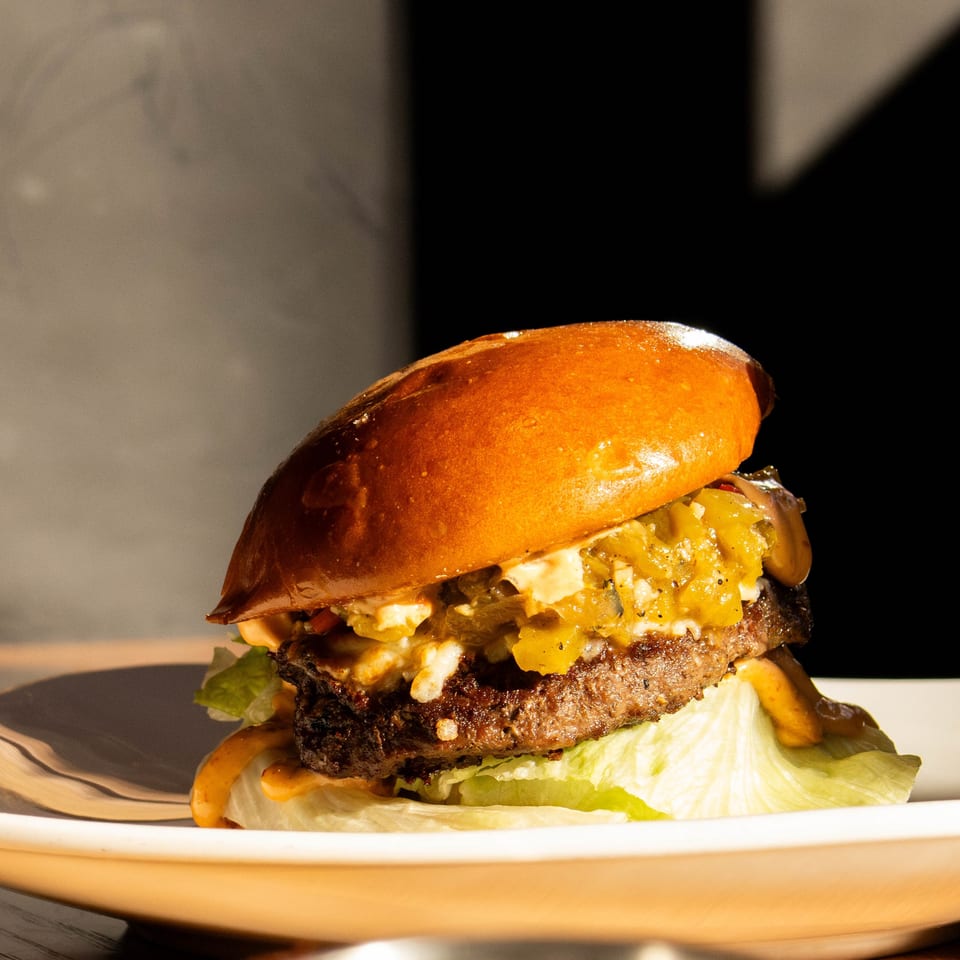 Close-up of a gourmet burger with green chili relish, cheese, lettuce, and special sauce on a white plate.
