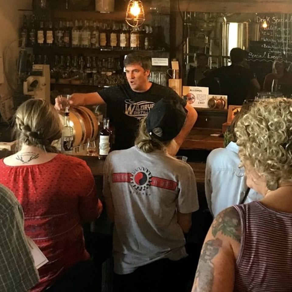 Bartender at Wildrye Distillery serves drinks to customers at a rustic bar.